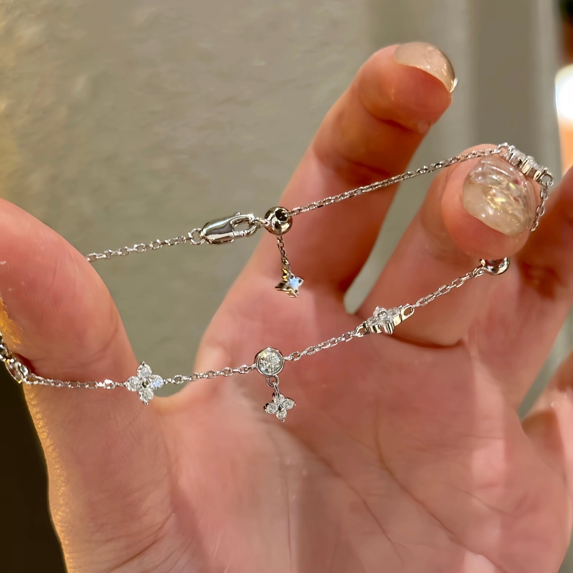 A hand holding a 925 sterling silver clover bracelet, demonstrating the innovative adjustable sliding bolo clasp for a perfect fit.
