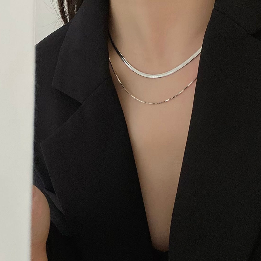 Close-up of a person wearing two silver necklaces against a black background