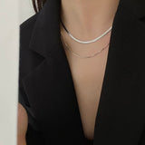 Close-up of a person wearing two silver necklaces against a black background