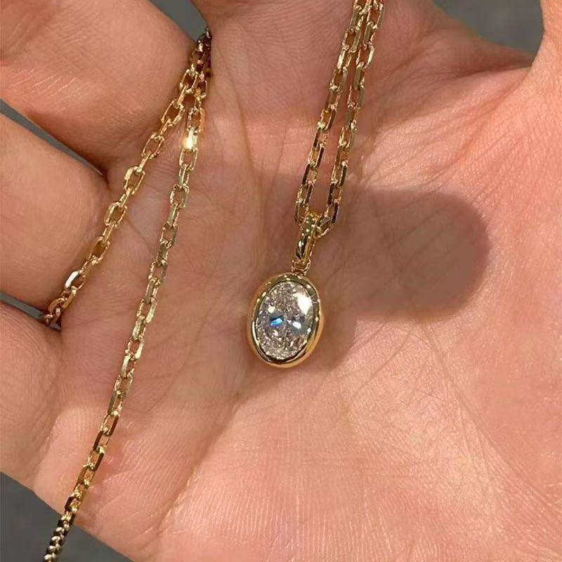 The solid 18K gold oval diamond pendant and chain resting in a hand, highlighting the premium craftsmanship.