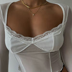 A woman wearing a trendy white sheer long-sleeve top with a sweetheart lace neckline, showcasing a layered gold herringbone chain and a cubic zirconia initial W necklace on her chest.