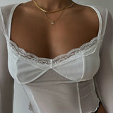 A woman wearing a trendy white sheer long-sleeve top with a sweetheart lace neckline, showcasing a layered gold herringbone chain and a cubic zirconia initial W necklace on her chest.