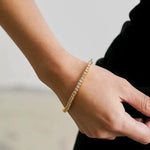 Side view detail of a gold tennis bracelet on a wrist, emphasizing the craftsmanship and diamond-like shine.