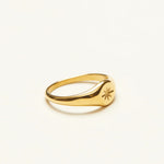 Side angle of a delicate gold signet ring, highlighting the slender band and the engraved star detail on the smooth face.