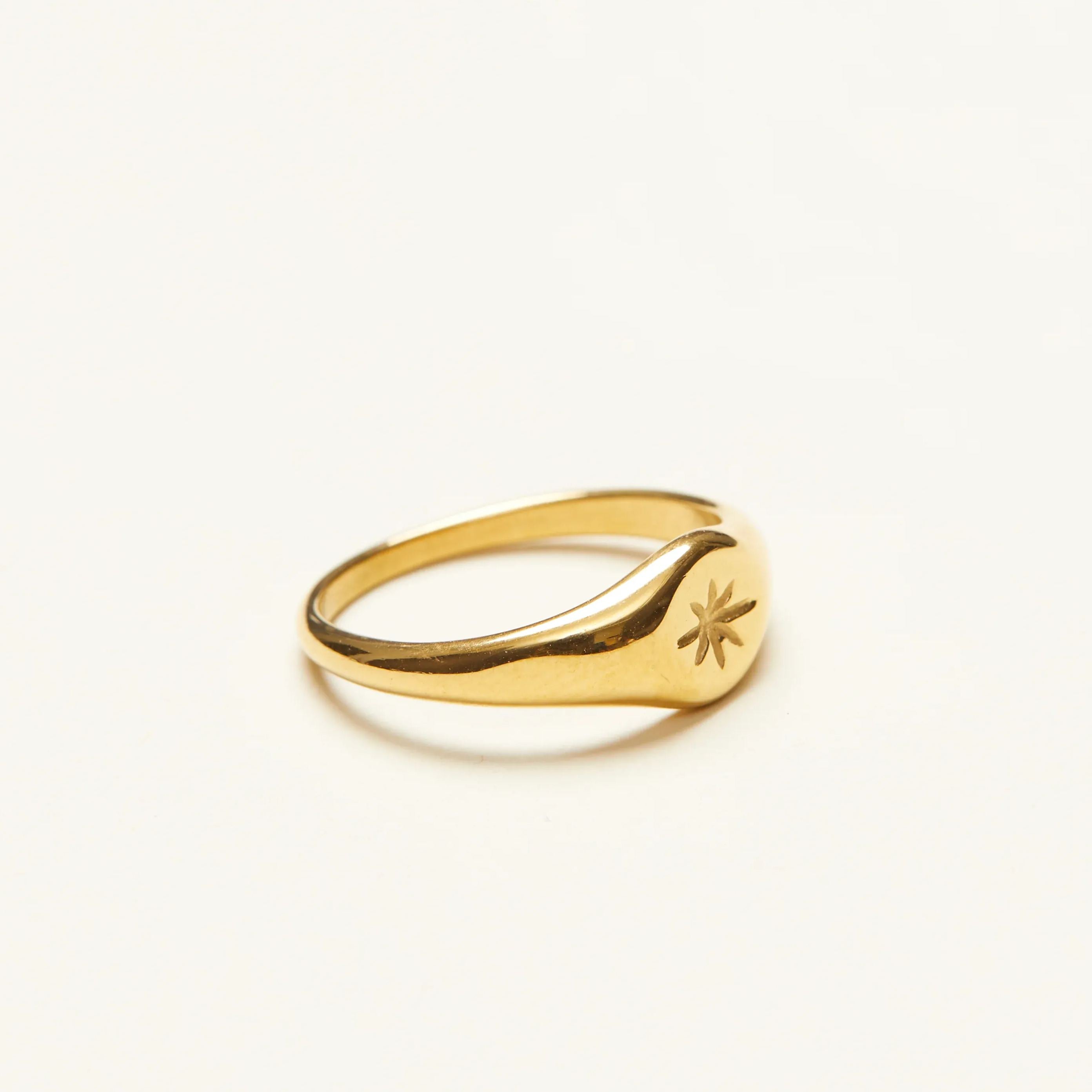 Side angle of a delicate gold signet ring, highlighting the slender band and the engraved star detail on the smooth face.