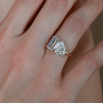 A 3.70 ctw Toi et Moi ring featuring a brilliant emerald-cut and pear-cut lab diamond on a model's finger in 18K gold.