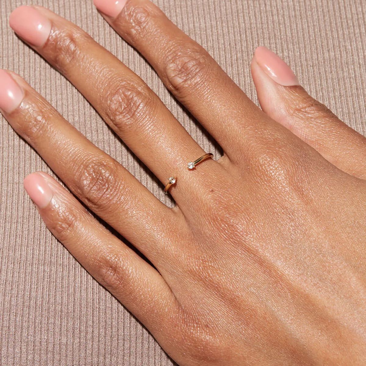 Top-down view of a delicate gold open ring on a finger, highlighting the unique gap between the two brilliant stones.