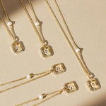 Full view of the vintage gold sunburst initial necklace with a freshwater pearl, laid flat on draped white material.