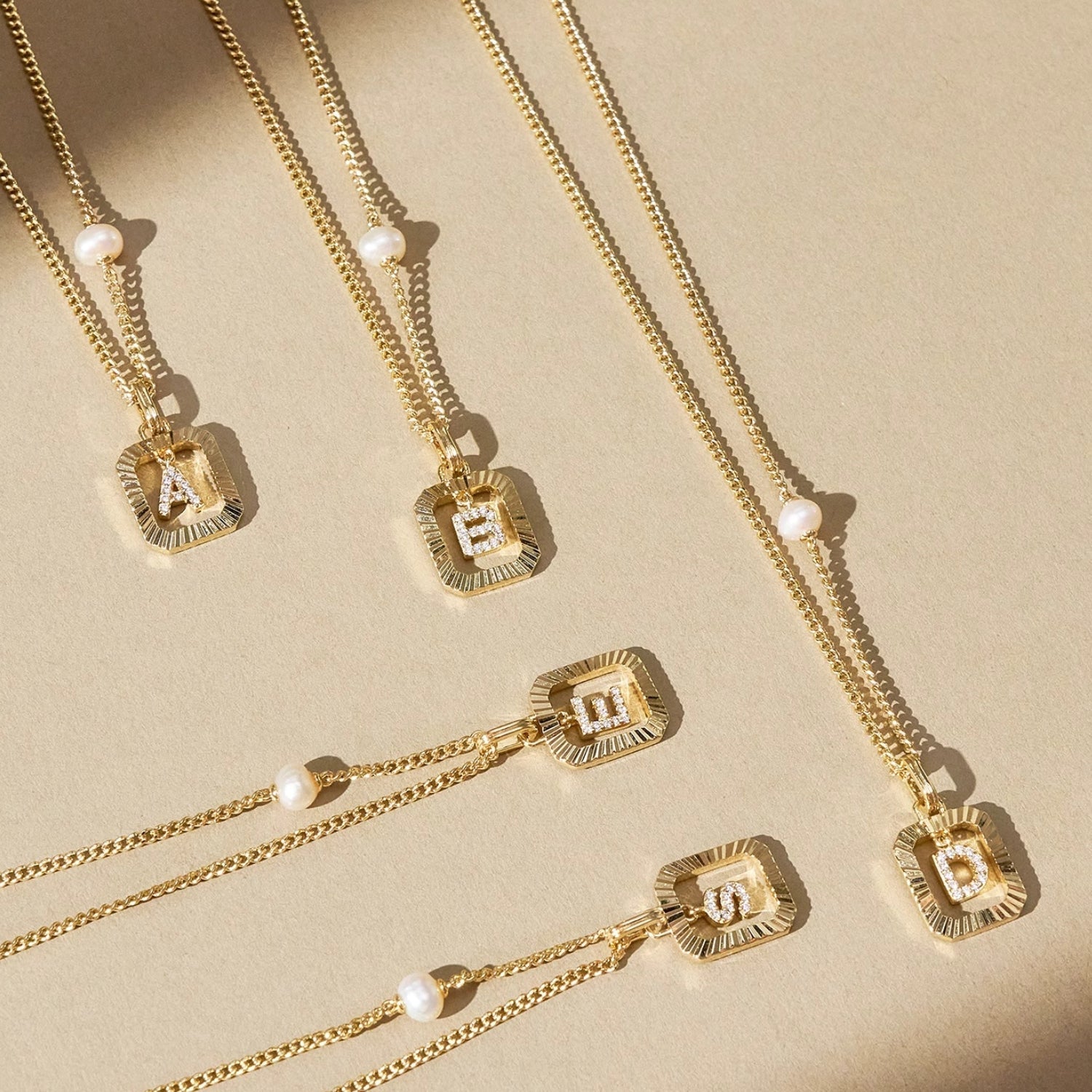 Full view of the vintage gold sunburst initial necklace with a freshwater pearl, laid flat on draped white material.