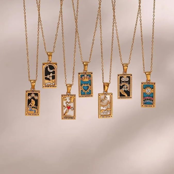 A collection of seven different 18K gold plated enamel tarot card necklaces hanging against a soft background, including The Star, Knight of Cups, The Lovers, The Empress, The Moon, The Magician, and The Sun.