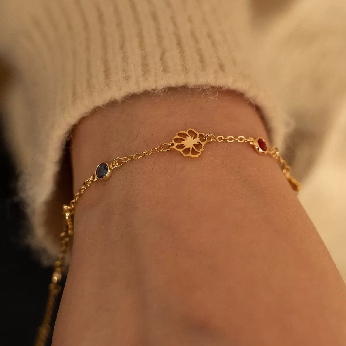 A woman wearing a delicate gold custom family garden bracelet, adjusting it on her wrist in warm, cozy lighting.