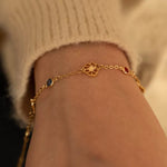 A woman wearing a delicate gold custom family garden bracelet, adjusting it on her wrist in warm, cozy lighting.