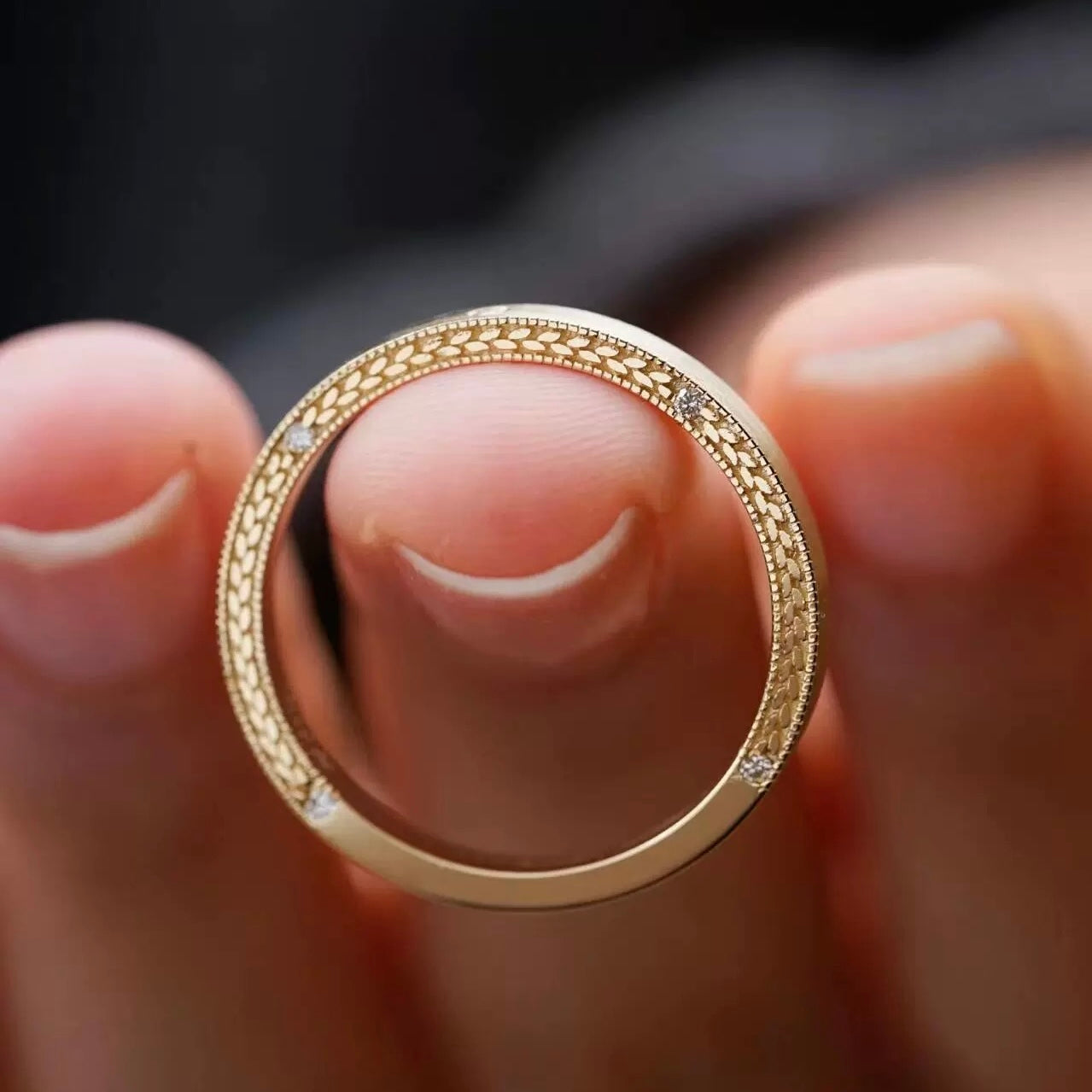 Close-up detail of the intricate wheat and laurel pattern etched along the edge of an 18K gold-plated couple ring.