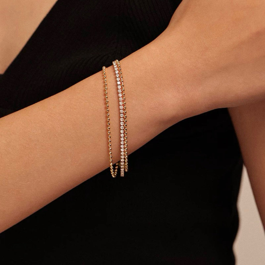 A woman with her hand resting across her body, elegantly displaying a shiny gold triple-strand bracelet with micro-pave crystals against her black garment.
