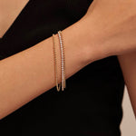 A woman with her hand resting across her body, elegantly displaying a shiny gold triple-strand bracelet with micro-pave crystals against her black garment.