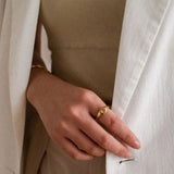 A woman wearing a beige top and a white blazer, elegantly showcasing a gold starburst signet ring on her ring finger.